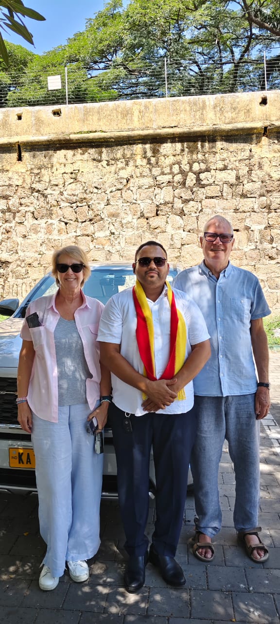 Shajid Mohammed, wearing a ceremonial shawl, standing with two guests beside his car at a South Indian fort